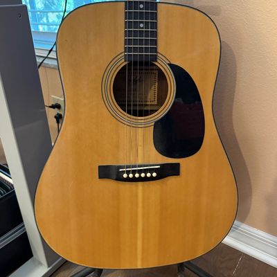 Vintage Regal acoustic dreadnought guitar with a natural finish top, black pickguard, and rosewood fretboard, displayed on a black stand.