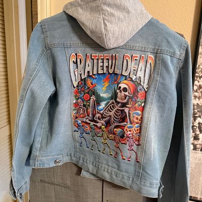 Light-wash denim jacket featuring a grey knit hood and a large, colorful Grateful Dead graphic patch on the back and sleeves