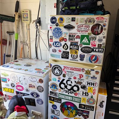 A compact refrigerator and a chest freezer, both heavily decorated with various colorful stickers.