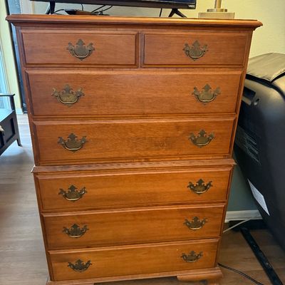 Vintage cherry wood tallboy dresser in a Colonial Revival style, featuring bracket feet and ornate brass batwing drawer pulls.