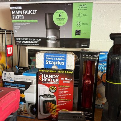 Assorted household items in original packaging, including an AO Smith under-sink water filter, a Handy Heater, a smart camera light bulb,...