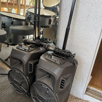 Two Tzumi X-Bass portable karaoke speakers with telescoping handles, wheels, and wired microphones.