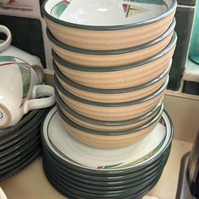 Stack of vintage stoneware bowls and plates featuring a southwest-inspired design with green trim and textured tan exteriors.