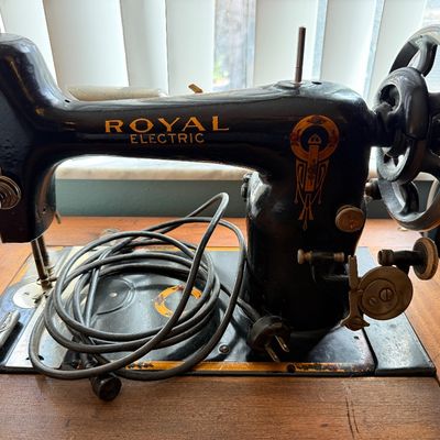 Vintage Royal Electric sewing machine with black cast iron body, gold Art Deco decals, and integrated power cord, mounted on a wooden...