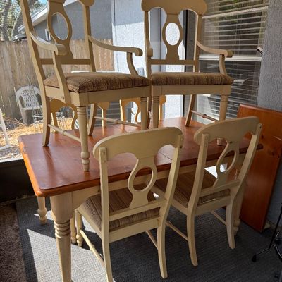 Country-style dining set featuring a wooden table with turned legs and a natural finish top, paired with four cream-painted chairs with...