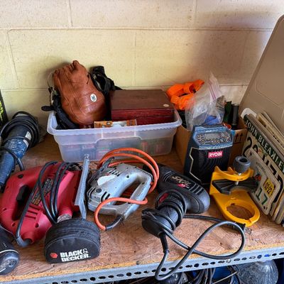 Assortment of power tools and garage items, including a Skil drill, a red jigsaw, a Ryobi radio, and vintage license plates.