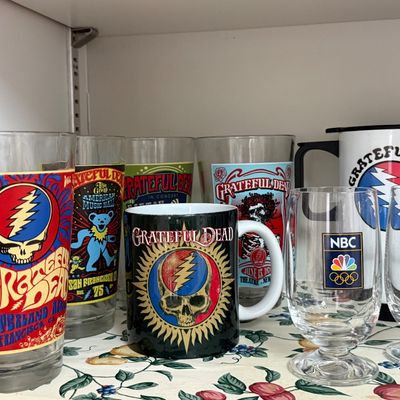 Collection of Grateful Dead memorabilia glassware, including pint glasses, a ceramic mug, and a travel mug, alongside two NBC Olympics...