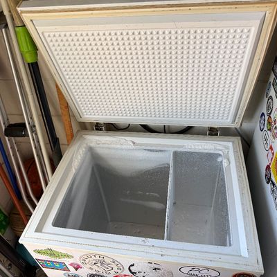 White chest freezer shown open, featuring a divided interior compartment and various stickers on the exterior.