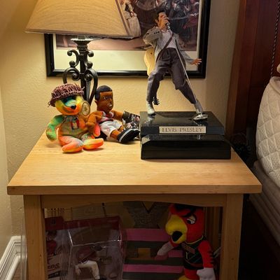 Light wood nightstand featuring an Elvis Presley figurine phone, a Grateful Dead bear plush, and sports memorabilia including a Craig...