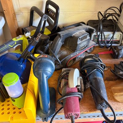Assortment of used power tools and garage equipment, including a Craftsman belt sander, a Ryobi chainsaw, a battery charger, and various...