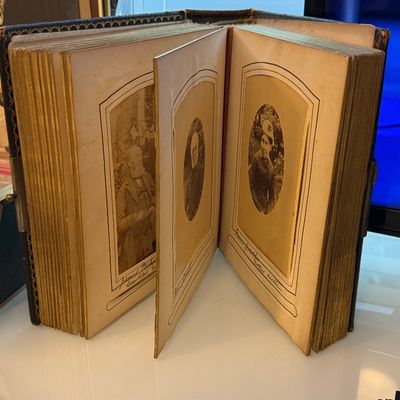 Antique Victorian photo album with gold-gilded edges, featuring cabinet cards and handwritten inscriptions beneath the portraits.