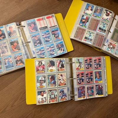Three yellow three-ring binders filled with vintage baseball and football trading cards from the late 1970s and early 1980s, organized in...