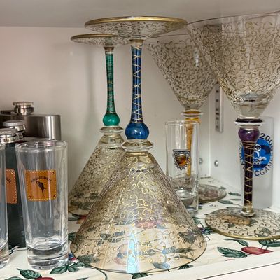 Collection of hand-painted martini glasses with intricate gold scrollwork and colorful stems, displayed alongside Margaritaville shot...