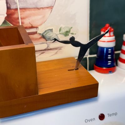 Vintage wooden matchbox holder with a metal gymnast-shaped match striker, shown alongside a pair of ceramic lighthouse salt and pepper...