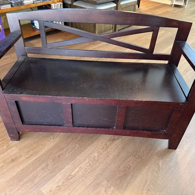 Dark-stained wooden storage bench featuring an X-back design, armrests, and a lift-top seat. 