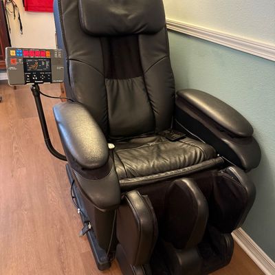 Panasonic black leather massage chair featuring a mounted control panel, padded headrest, and integrated leg massagers.