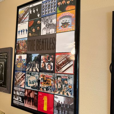 Framed poster featuring a collage of The Beatles album covers, housed in a simple black frame.