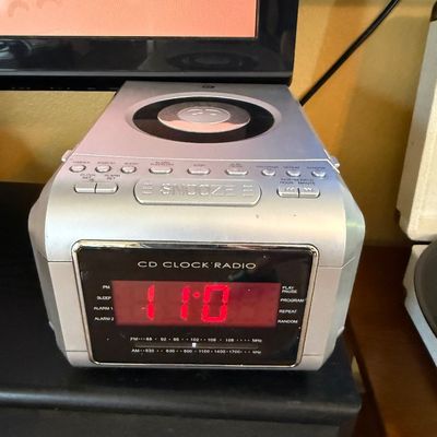 Vintage silver-toned CD clock radio with a red digital LED display and top-loading CD player.