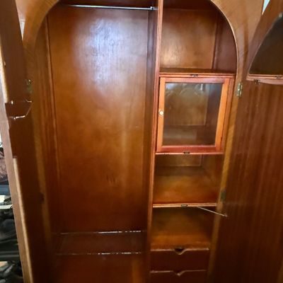 Vintage Art Deco style wooden wardrobe featuring an arched interior frame, a hanging rod on the left, and a combination of shelves, a...