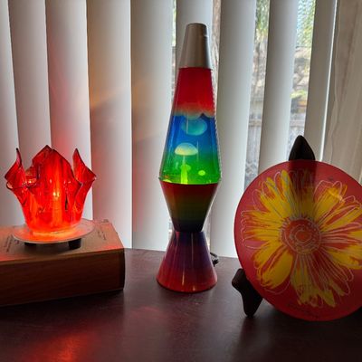 Retro-style home decor items including a red art glass lamp, a rainbow-colored lava lamp, and a decorative glass plate featuring a yellow...