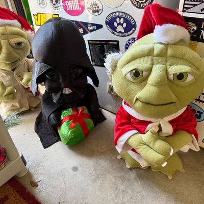Three Star Wars plush holiday decorations, including two Yoda figures in Santa hats and one Darth Vader holding a green present.