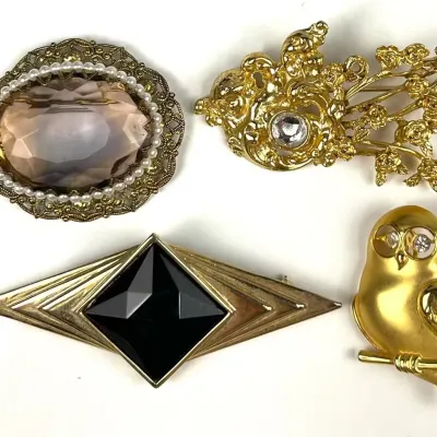 Collection of four vintage gold-tone brooches, including a faux pearl and smoky quartz-style cameo, an ornate floral design with a...