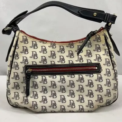 Dooney & Bourke signature monogram shoulder bag in cream and black canvas with black leather trim and a zippered front pocket.
