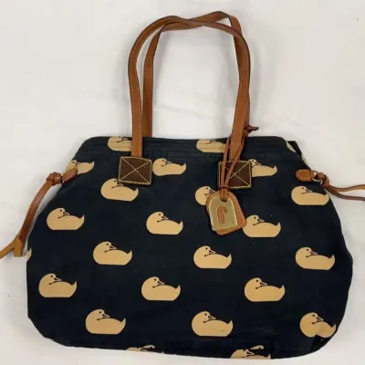 Dooney & Bourke canvas tote bag featuring a repeating duck pattern on a black background with tan leather handles and trim.