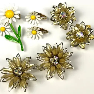 Assortment of vintage mid-century floral costume jewelry, including enamel daisy brooches and clip-on earrings, alongside gold-tone...