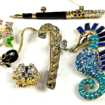 Collection of vintage costume jewelry brooches, including a rhinestone-encrusted seahorse, a fountain pen, a candy cane, a mouse, a...