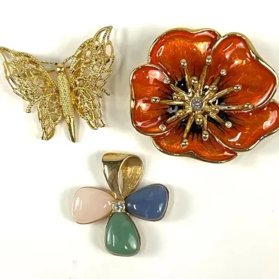 Vintage costume jewelry trio including a gold-tone filigree butterfly brooch, a vibrant orange enamel flower brooch with rhinestone...