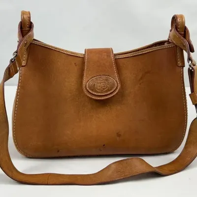 Vintage Dooney & Bourke tan leather shoulder bag featuring an embossed logo on the front flap and an adjustable strap, showing some...