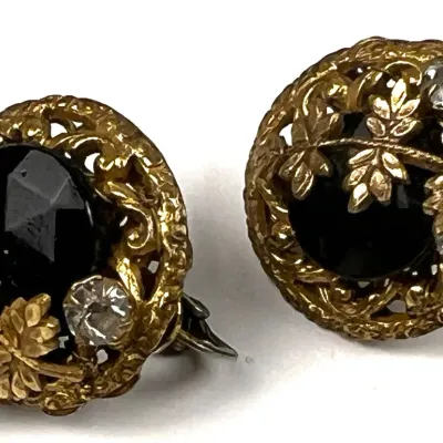 Vintage gold-tone filigree clip-on earrings featuring large faceted black glass cabochons accented with small clear rhinestones and leaf...