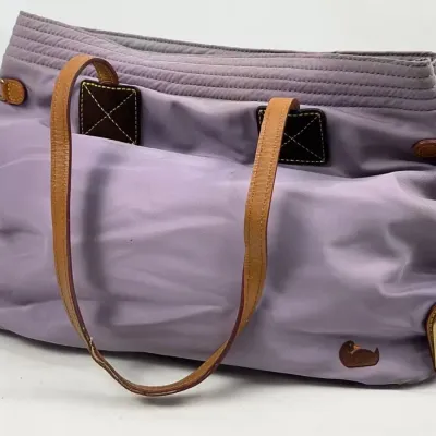 Dooney & Bourke lavender nylon shoulder bag featuring tan leather straps, a signature duck logo patch, and a gold-tone metal logo...