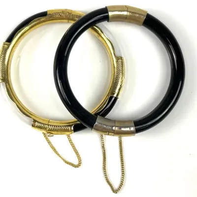 Pair of vintage hinged bangle bracelets, one featuring a black band with gold-tone metal accents and the other featuring a gold-tone...