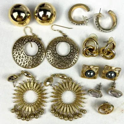 Collection of vintage gold-tone fashion earrings, including large textured hoops, sunburst dangles, dome studs, and rhinestone-accented...