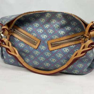 Dooney & Bourke signature monogram canvas handbag in blue and pink, featuring tan leather braided handles and dual front zipper pockets.