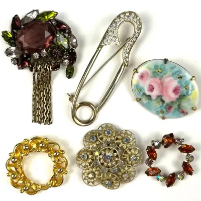 Collection of six vintage costume jewelry brooches, including a rhinestone-accented safety pin, a hand-painted floral porcelain cabochon,...