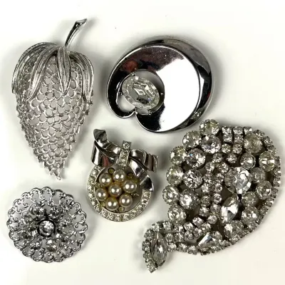 Collection of five vintage mid-century costume jewelry brooches, featuring silver-tone metal, rhinestones, faux pearls, and filigree...