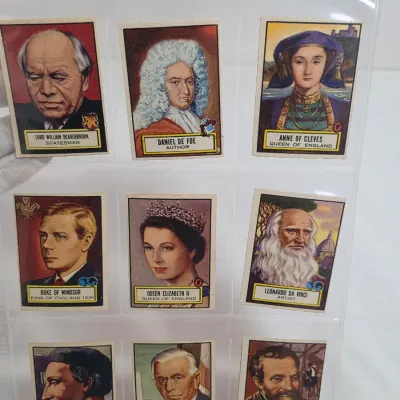 Sale Photo Thumbnail #8: Collection of vintage historical figure trading cards, including Queen Elizabeth II, Leonardo da Vinci, and Daniel Defoe, displayed in a plastic sleeve.