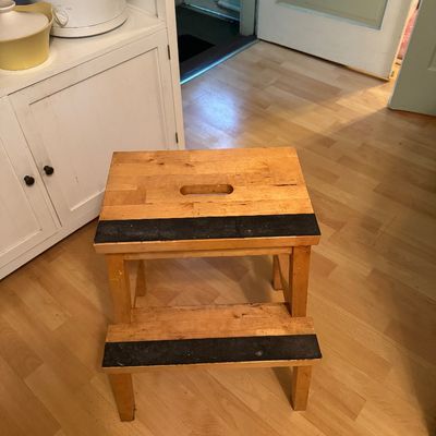 Two-step wooden step stool with black non-slip grip tape on each step and a built-in carrying handle on the top platform.