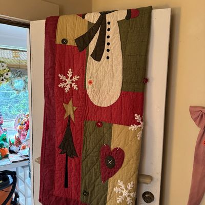 Handcrafted winter-themed quilted wall hanging or throw, featuring applique designs of a snowman, Christmas tree, heart, and snowflakes...