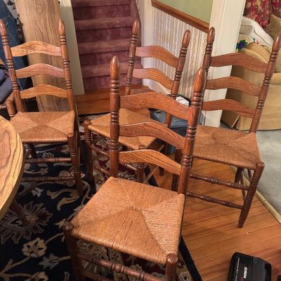 Set of four vintage oak ladder-back dining chairs featuring woven rush seats and turned wood details.