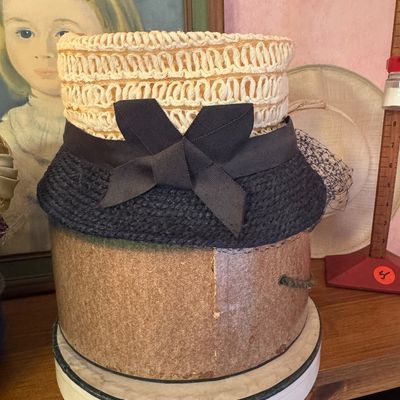 Vintage woven straw hat featuring a cream-colored crown, a dark navy or black brim, and a matching grosgrain ribbon bow, displayed on a...