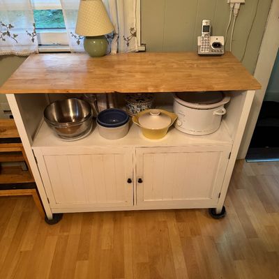 White painted wooden kitchen cart with a natural wood top, featuring an open shelf and a two-door lower cabinet.