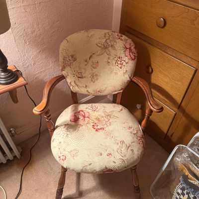 Vintage wooden armchair featuring floral upholstery in shades of cream, pink, and green, with turned legs and curved armrests.