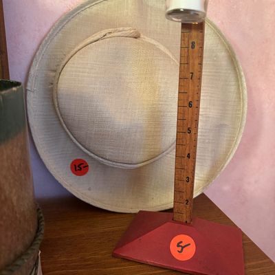 Vintage wooden rain gauge with a red base and a wide-brimmed straw hat in the background.