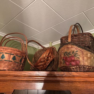 Collection of vintage woven baskets, including one with a stenciled pine tree design and another featuring a painted apple motif. 