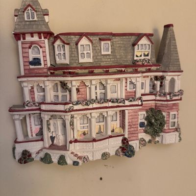 Three-dimensional resin wall plaque depicting a Victorian-style house with pink siding, grey roof shingles, and floral accents.