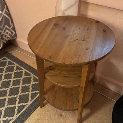 Three-tier round wooden side table with a natural finish, showing some light surface wear.